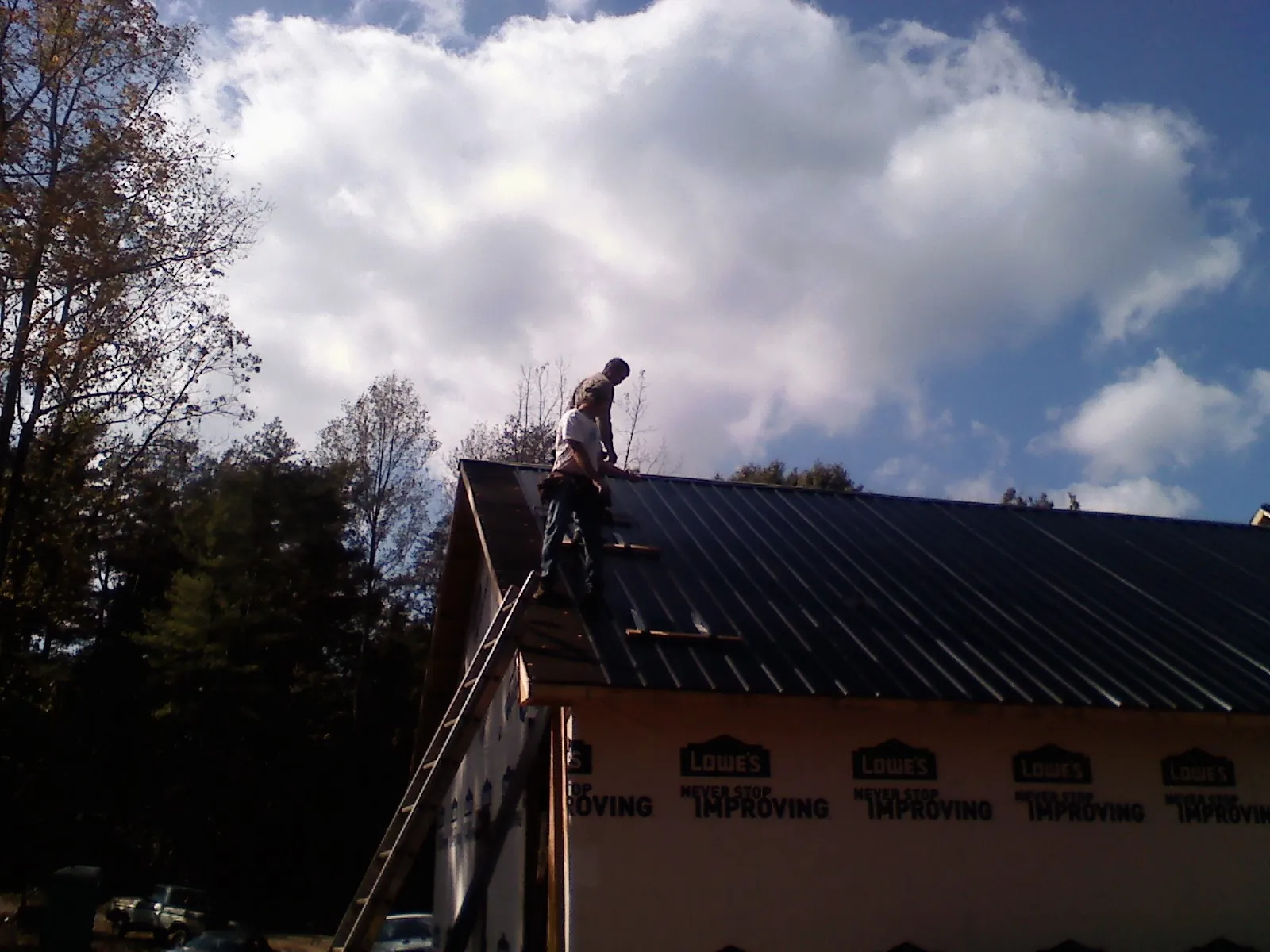 Roofer fastening dark metal panels high against a cloudy sky, from a Roof Inspection job in Carbondale